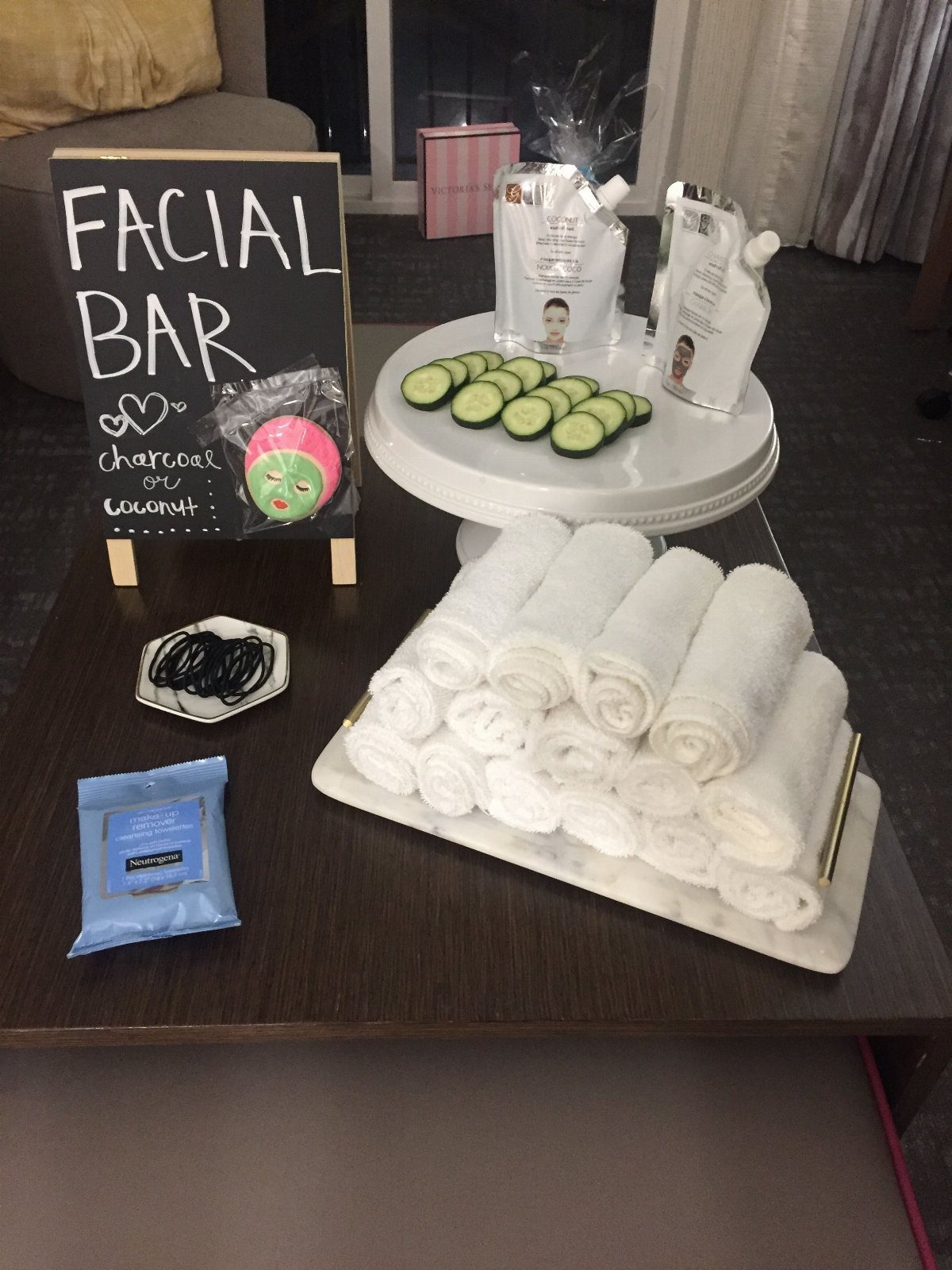A spa day facial bar setup with cucumbers, facial masks, and rolled white towels.