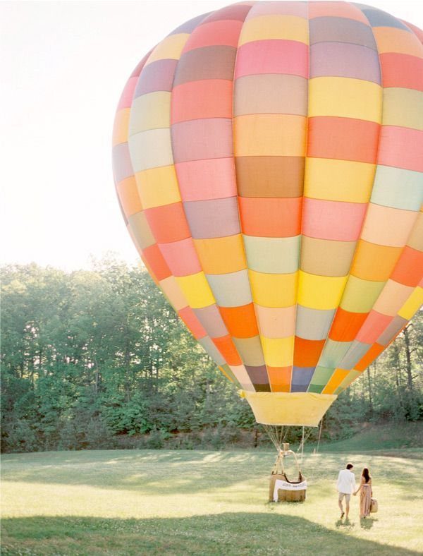 A colorful striped hot air balloon resting on a grassy field near a forest.