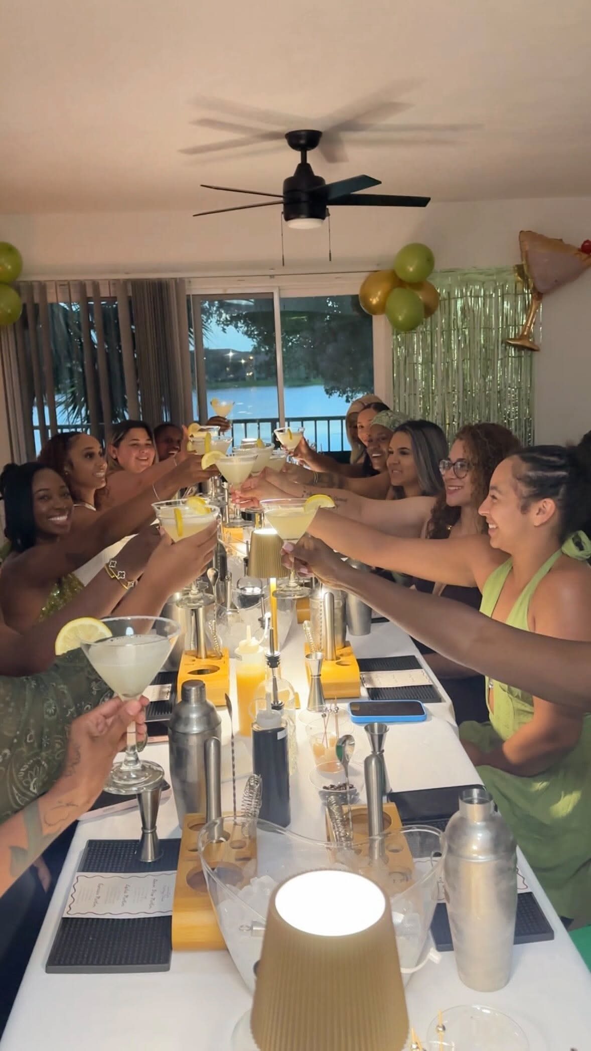Group of women smiling and raising cocktail glasses in a celebratory toast at a table.