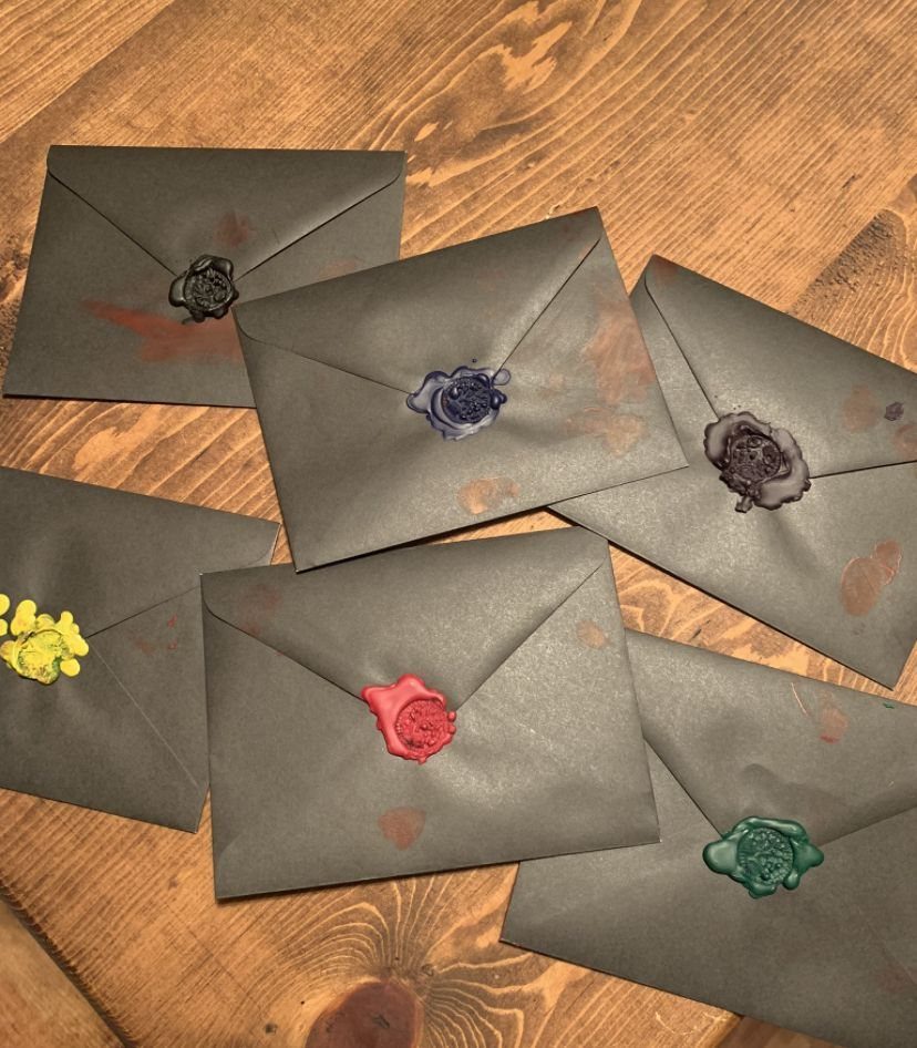 Six dark grey envelopes with colorful wax seals scattered on a wooden table.