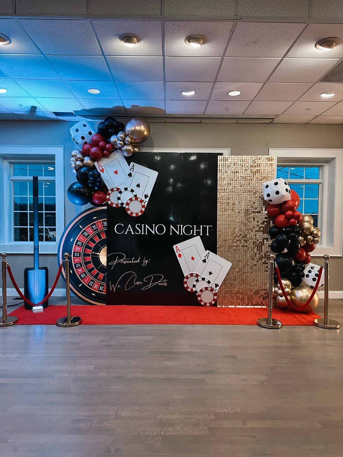 Casino night party backdrop with balloons, playing cards, dice, and a large roulette wheel.