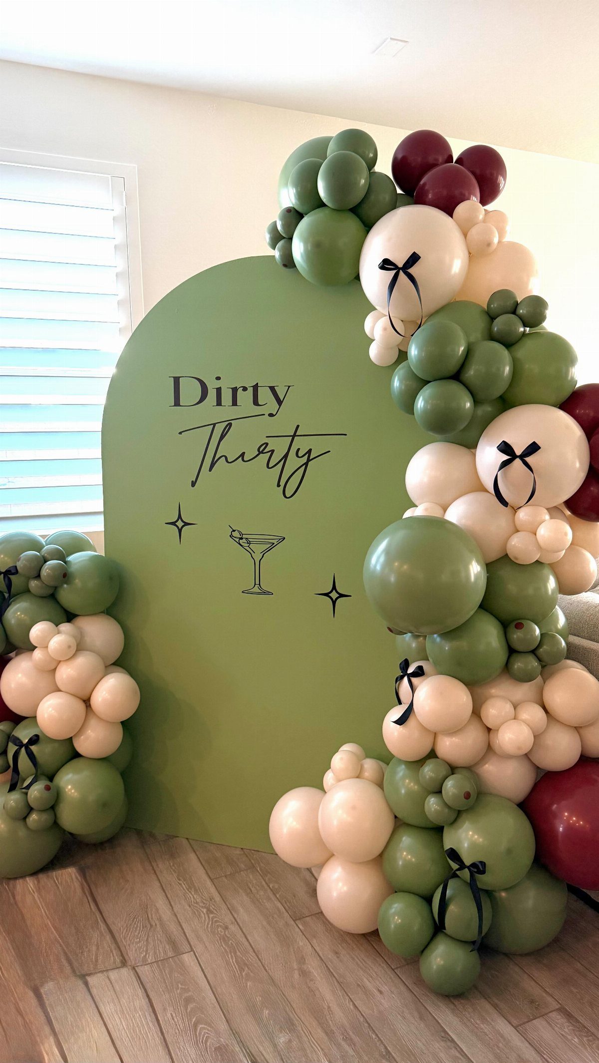 Sage green arched backdrop with balloon garland and Dirty Thirty text for a birthday party.