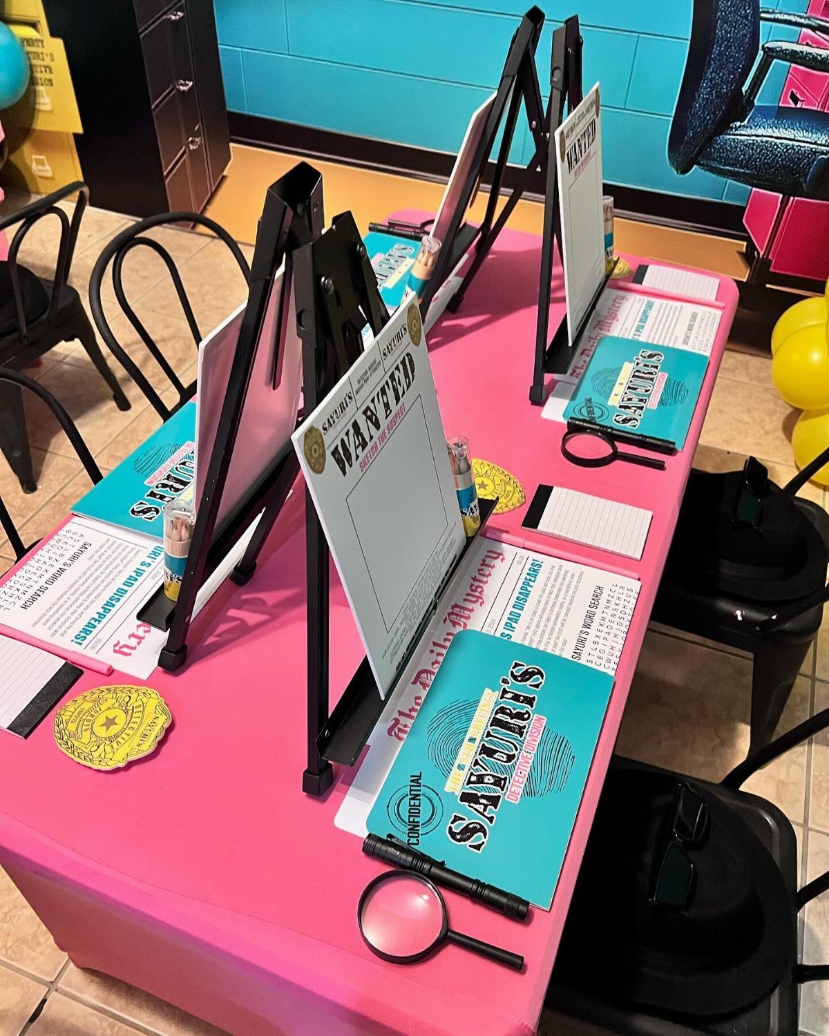 A pink table set with murder mystery party supplies, including magnifying glasses and wanted posters.