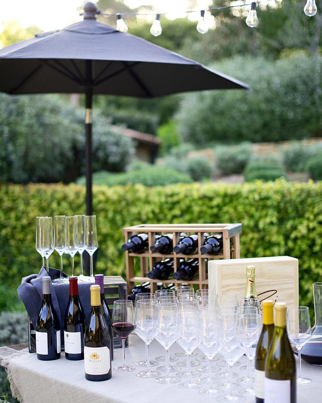 Wine bottles and various glassware arranged on a table in an outdoor garden setting.