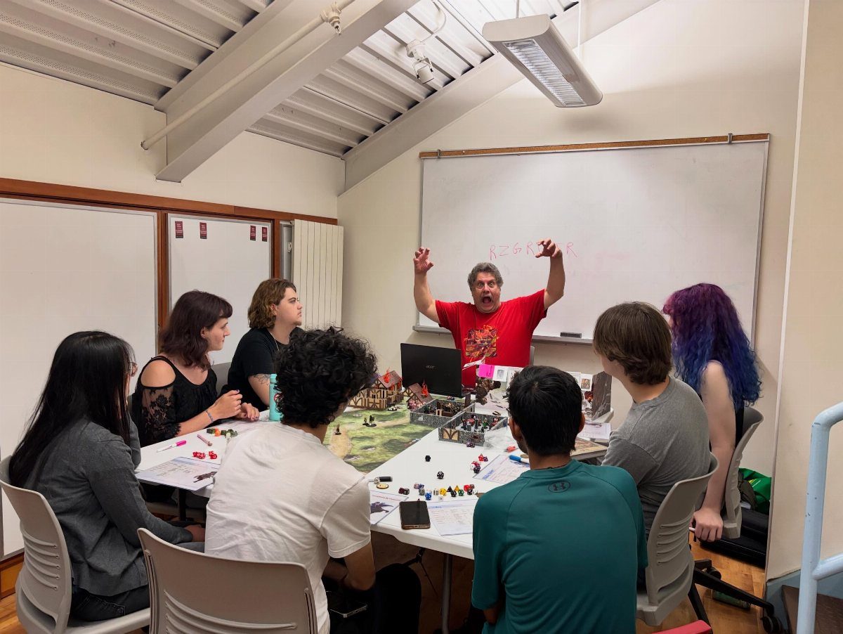 People gathered around a table playing a tabletop miniature wargame with small figures and terrain.