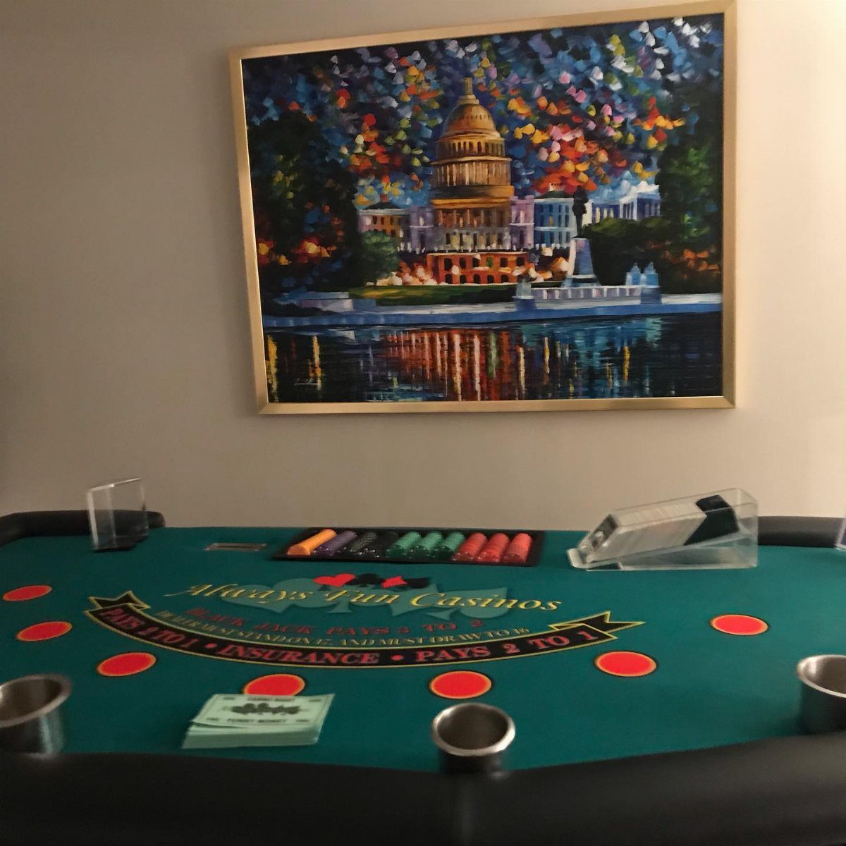 A green casino gaming table with red chips and cards in front of a painting.
