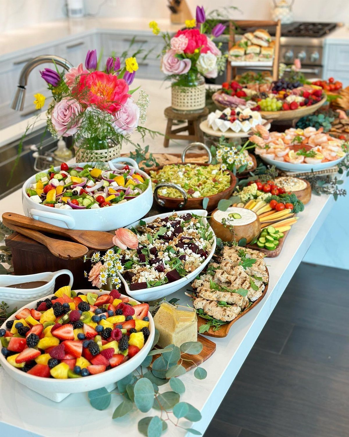 A large buffet spread featuring colorful fruit salads, shrimp, and various appetizers with floral arrangements.