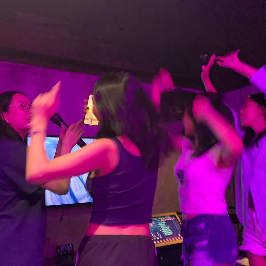 Young women dancing and singing with a microphone under bright purple lights.