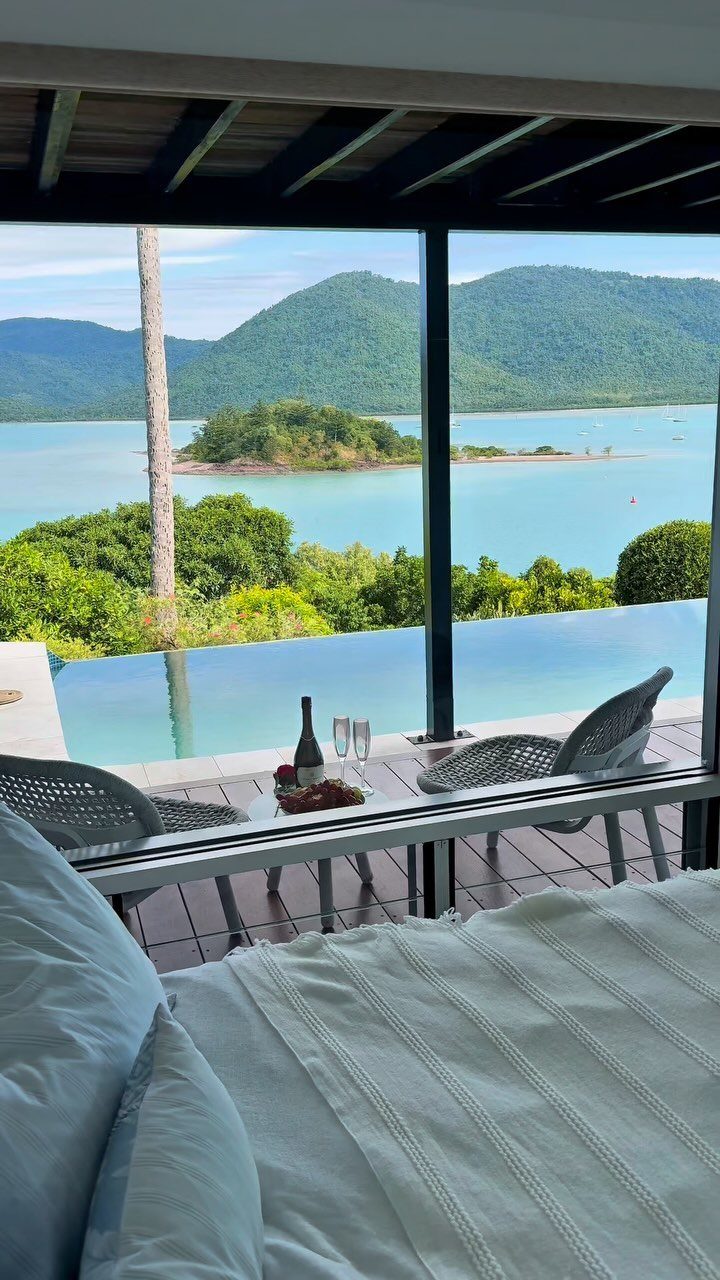 A luxury hotel balcony overlooking a tropical ocean view with champagne and an infinity pool.