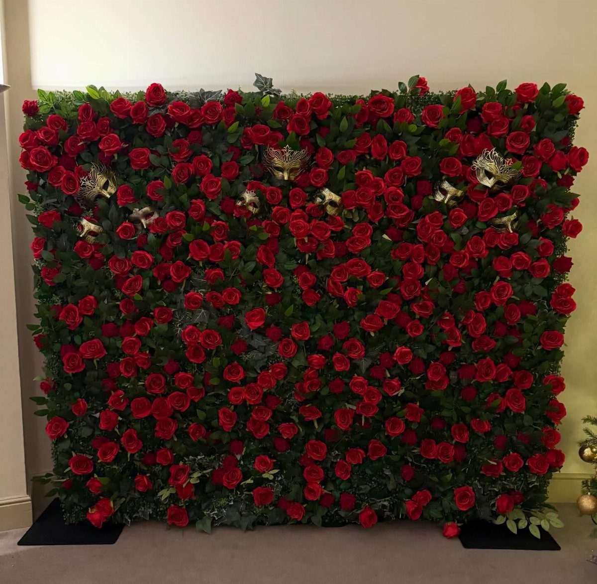 A lush wall of red roses decorated with several elegant gold masquerade masks.