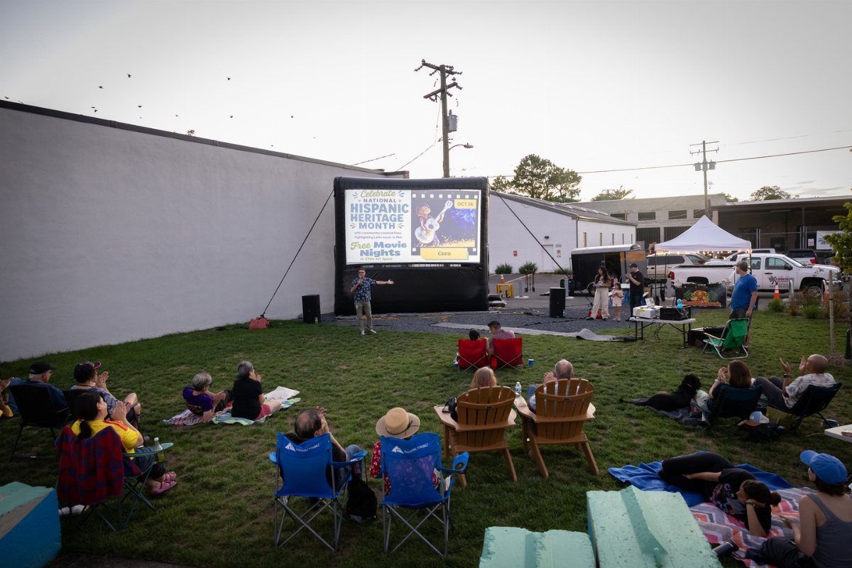 People sitting on grass and in chairs watching a movie on a large outdoor screen.