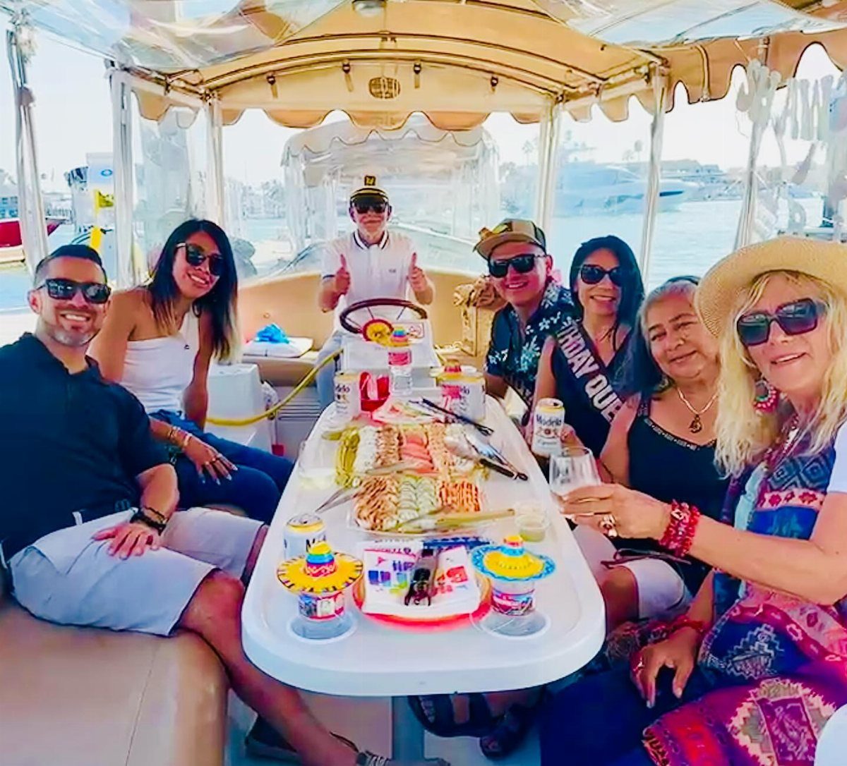 A group of friends smiling and enjoying drinks and snacks on a sunny boat ride.