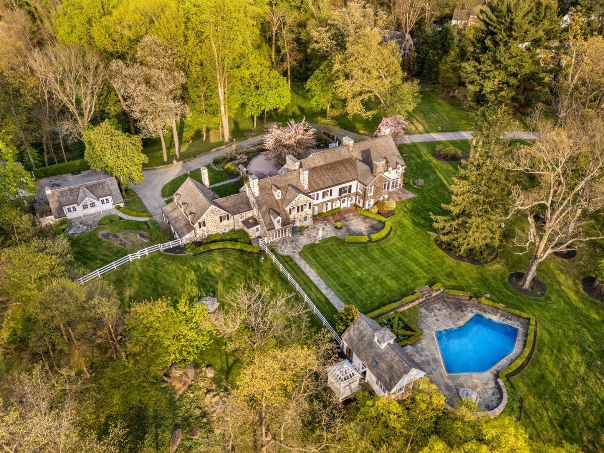Aerial view of a large stone mansion with green lawns, trees, and a swimming pool.