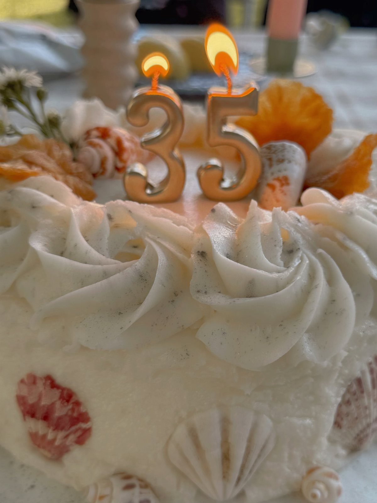 A white seashell-themed birthday cake with lit gold number 35 candles.