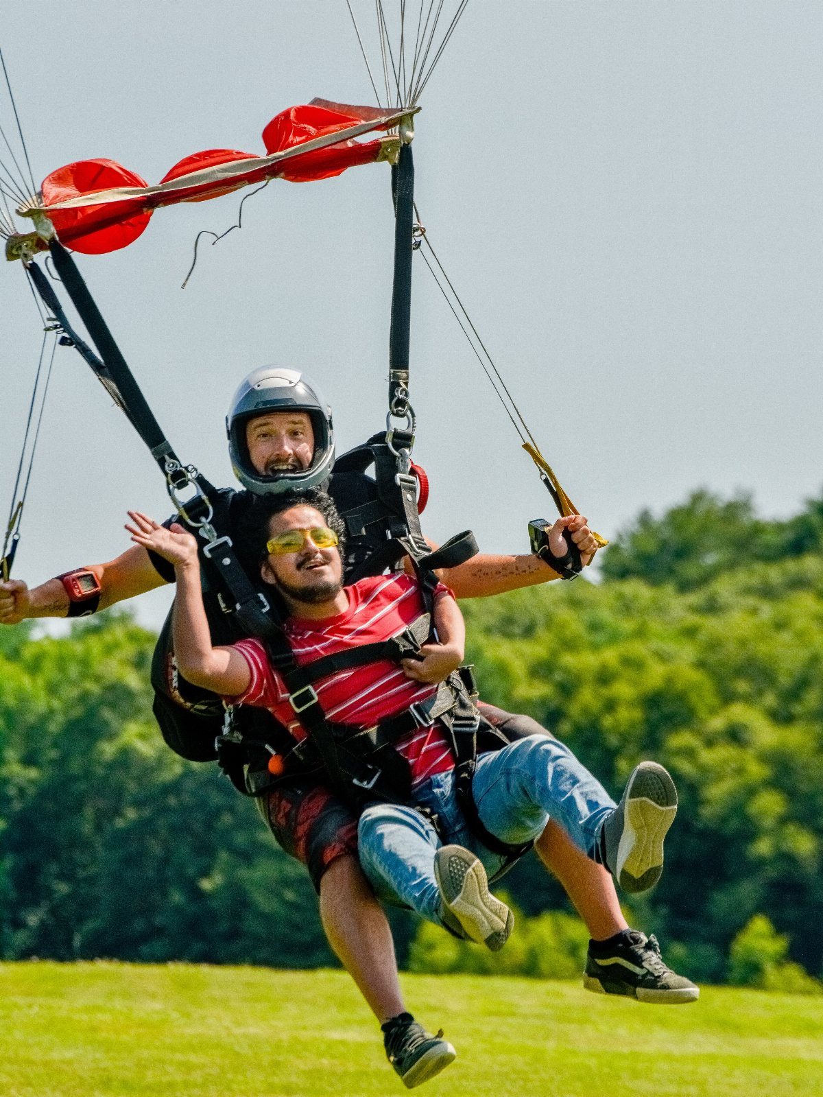Two men tandem paragliding over a lush green landscape under a clear sky.