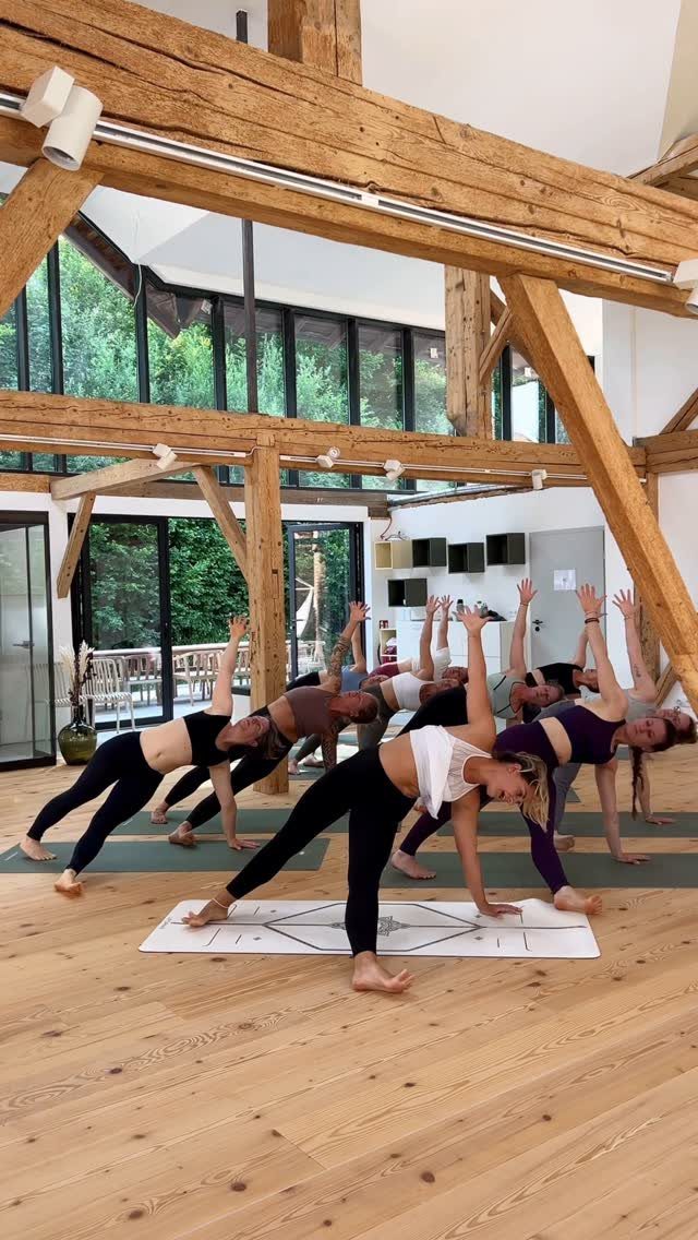 Women practicing side plank yoga poses in a bright, modern studio with wooden beams.