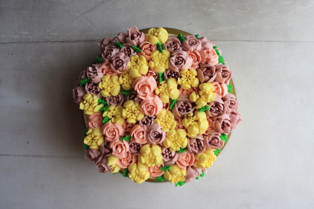 A round cake decorated with colorful buttercream frosting shaped like blooming flowers in pink, yellow, and lavender.