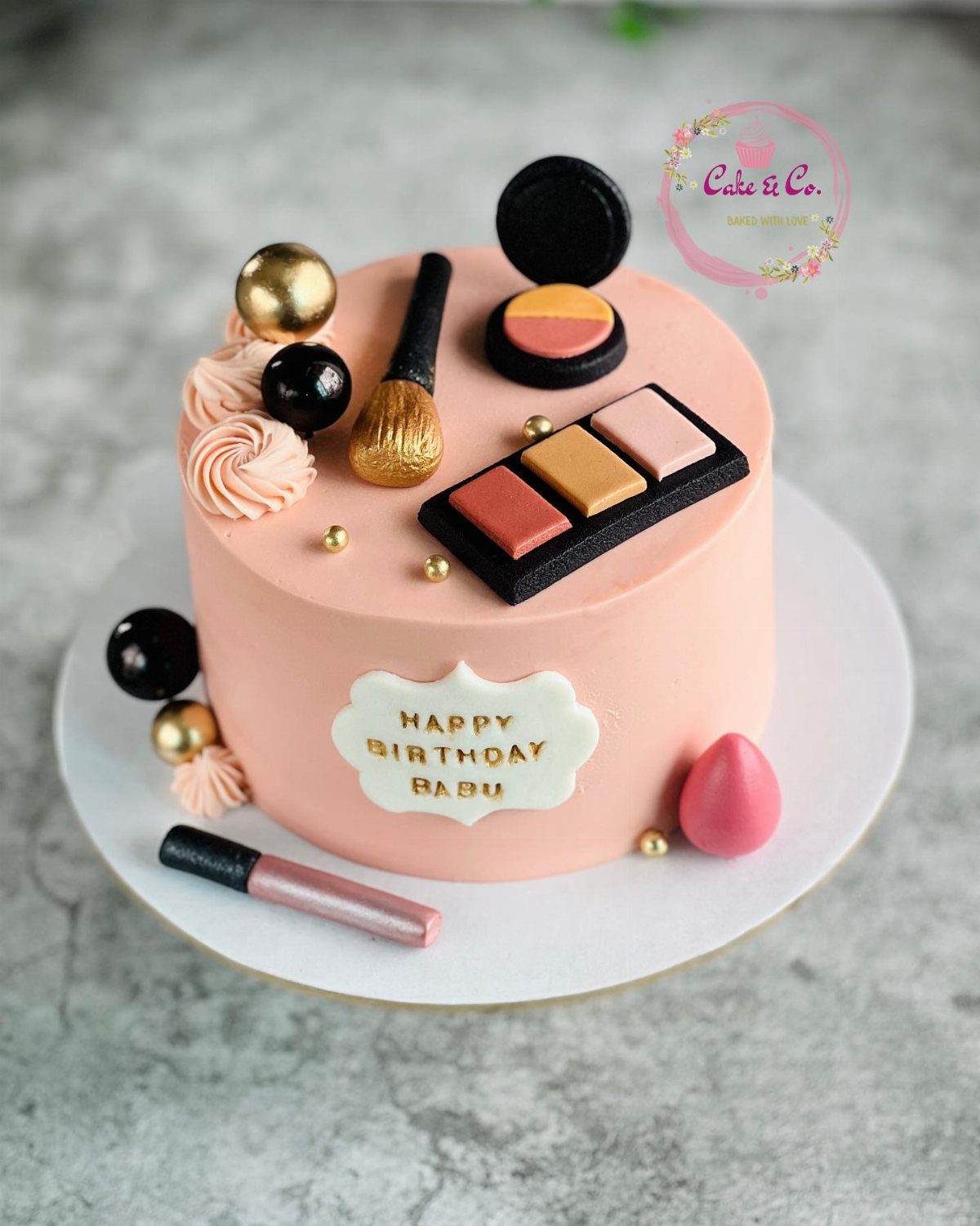 Peach-colored cake decorated with edible makeup items like an eyeshadow palette and gold brush.