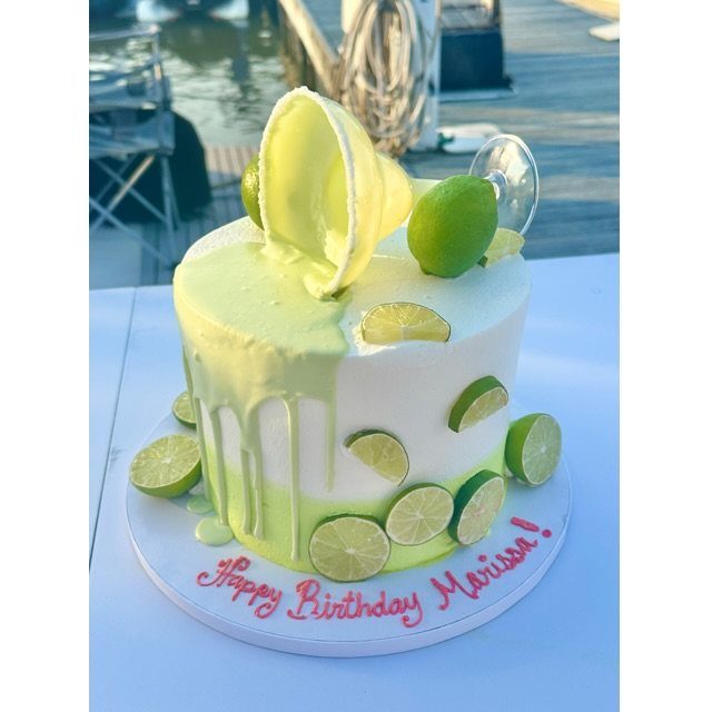 A white cake decorated with lime slices and lime-green frosting drips on a white table.