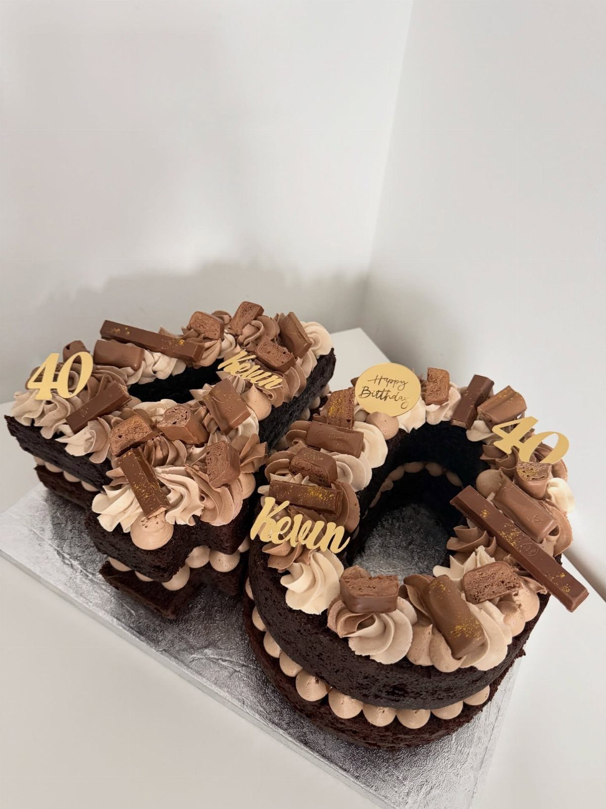 Two chocolate number 40 cakes decorated with chocolate frosting and various chocolate bar pieces.