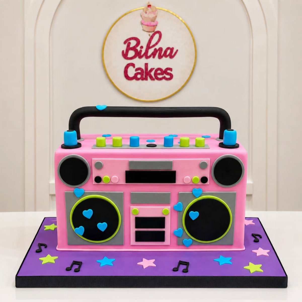 A pink boombox-shaped cake with colorful accents on a purple musical-themed base.