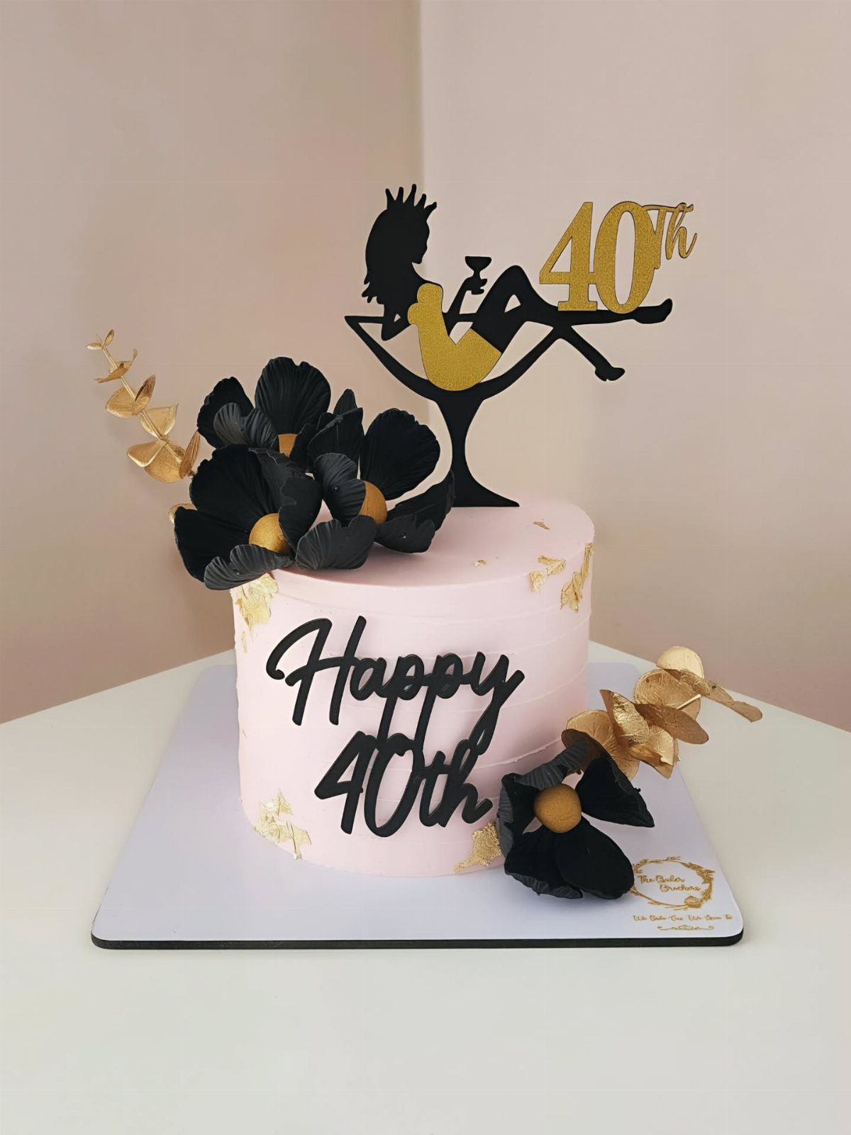 Pink cake with black flowers, gold leaf, and a woman silhouette topper celebrating a 40th birthday.