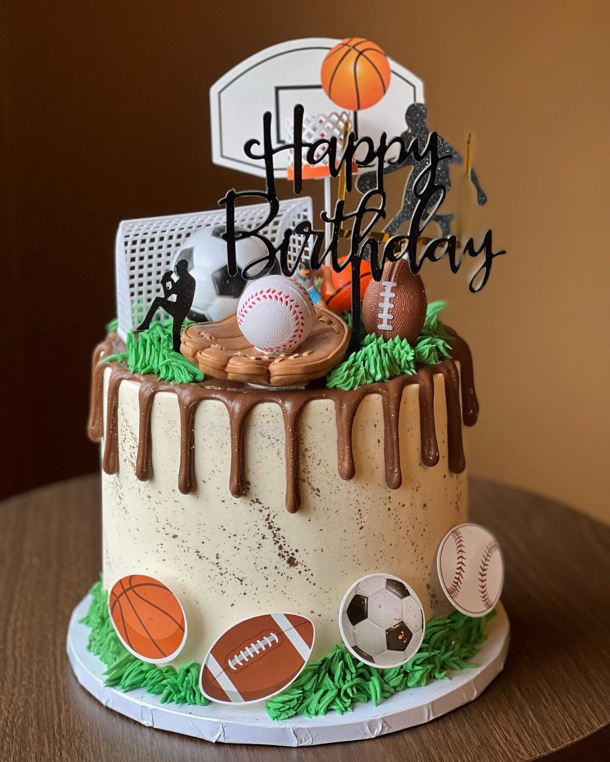 Sports themed birthday cake with chocolate drips and various ball decorations on white frosting.