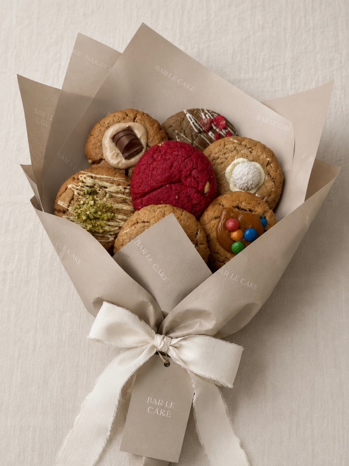 Assorted gourmet cookies arranged in a tan paper bouquet wrap with a white ribbon.