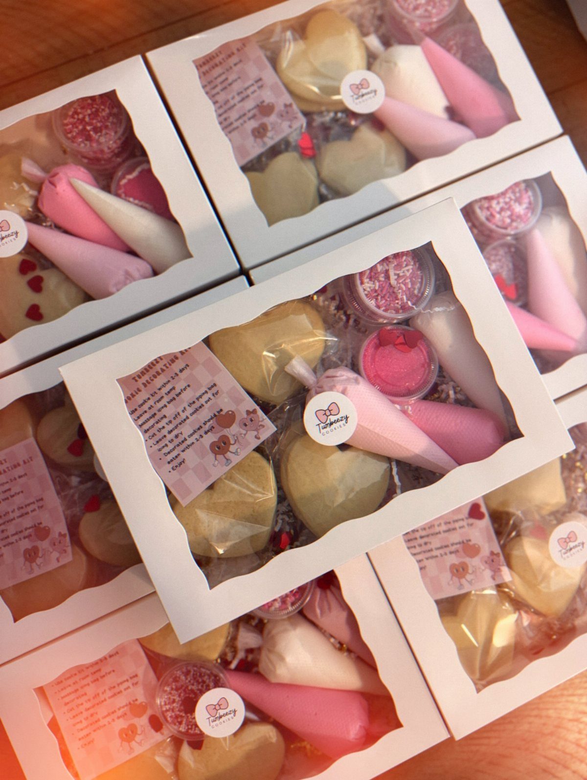 Multiple white boxes containing heart-shaped cookies, pink icing, and sprinkles for decorating kits.