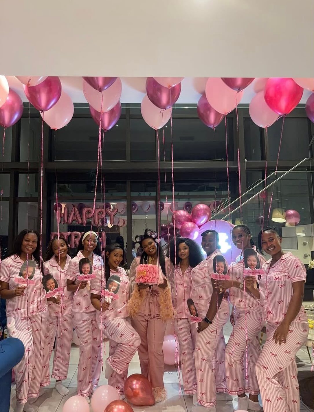 Group of women in matching pink striped pajamas posing with balloons and photos.