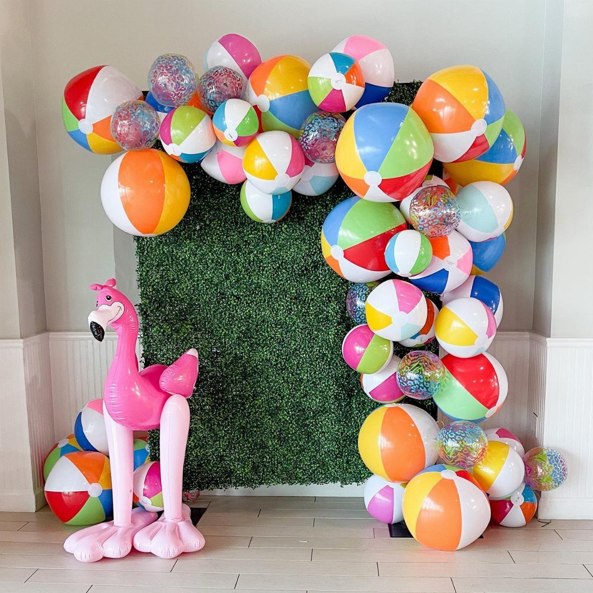 Colorful inflatable beach balls arranged around a green hedge wall with a pink flamingo.