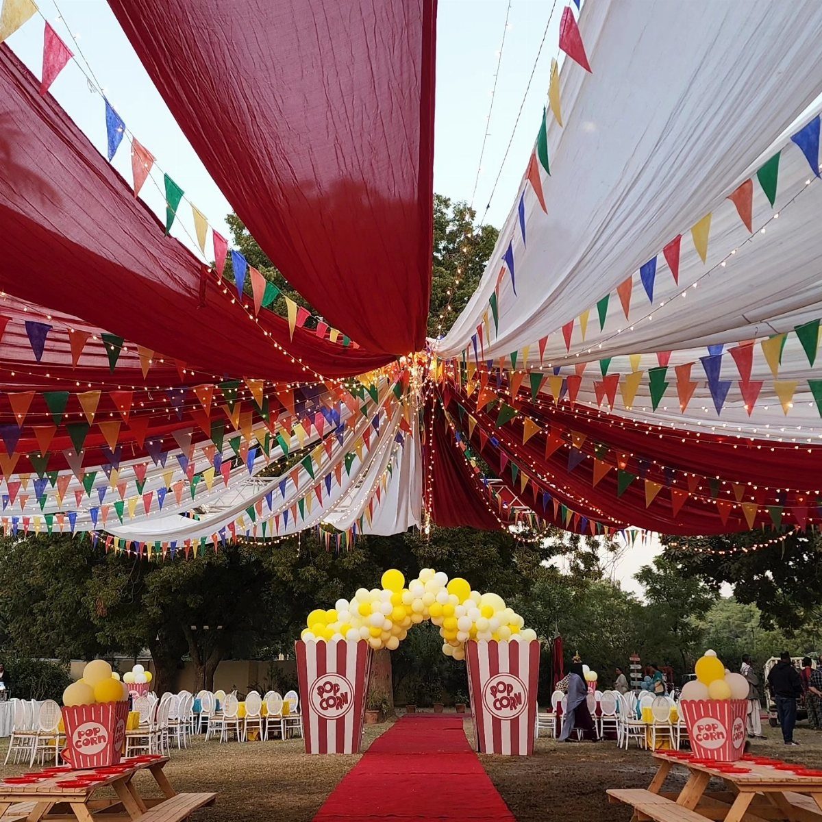 Red and white fabric canopies with colorful bunting and popcorn-themed balloon decorations over an outdoor party area.