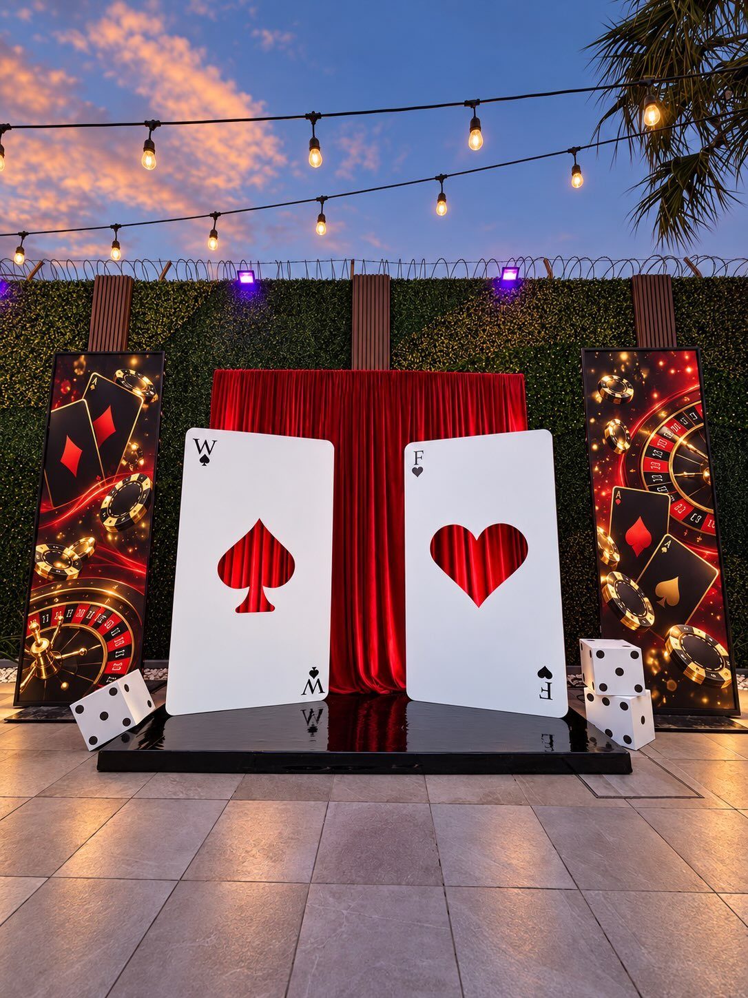 Casino-themed photo backdrop with oversized playing cards, red curtains, and roulette wheel panels outdoors.