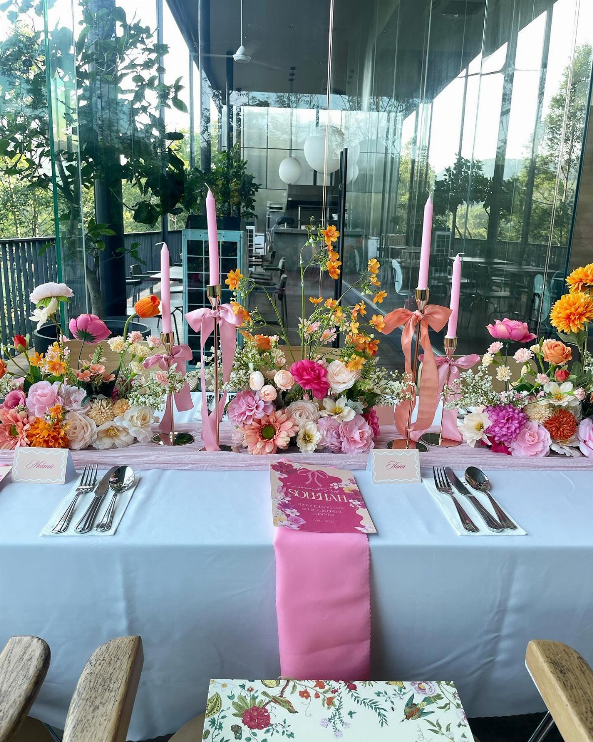 A decorated dining table featuring vibrant floral centerpieces and pink taper candles.