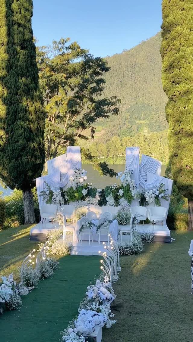 White floral wedding or event decor set on a green lawn with mountains in the background.