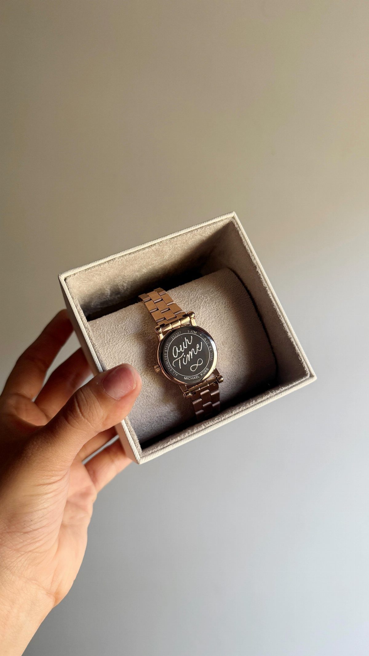 A hand holding an open velvet box containing a gold watch with custom text.