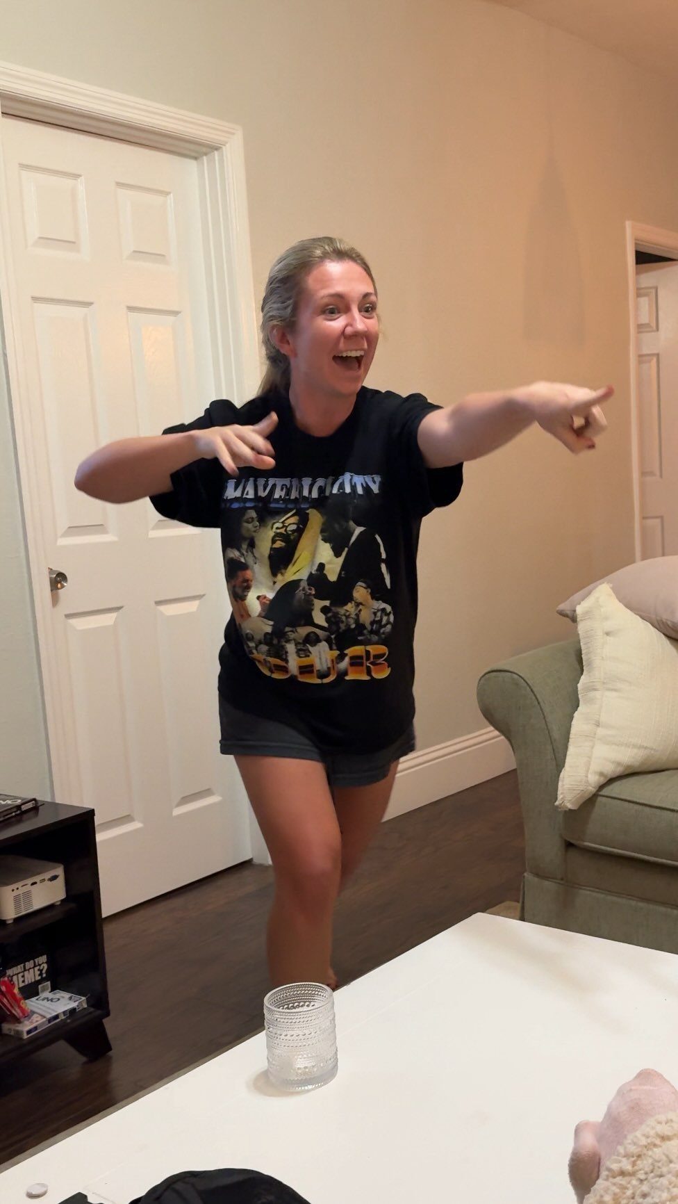 A laughing woman pointing with both hands while playing a game in a living room.