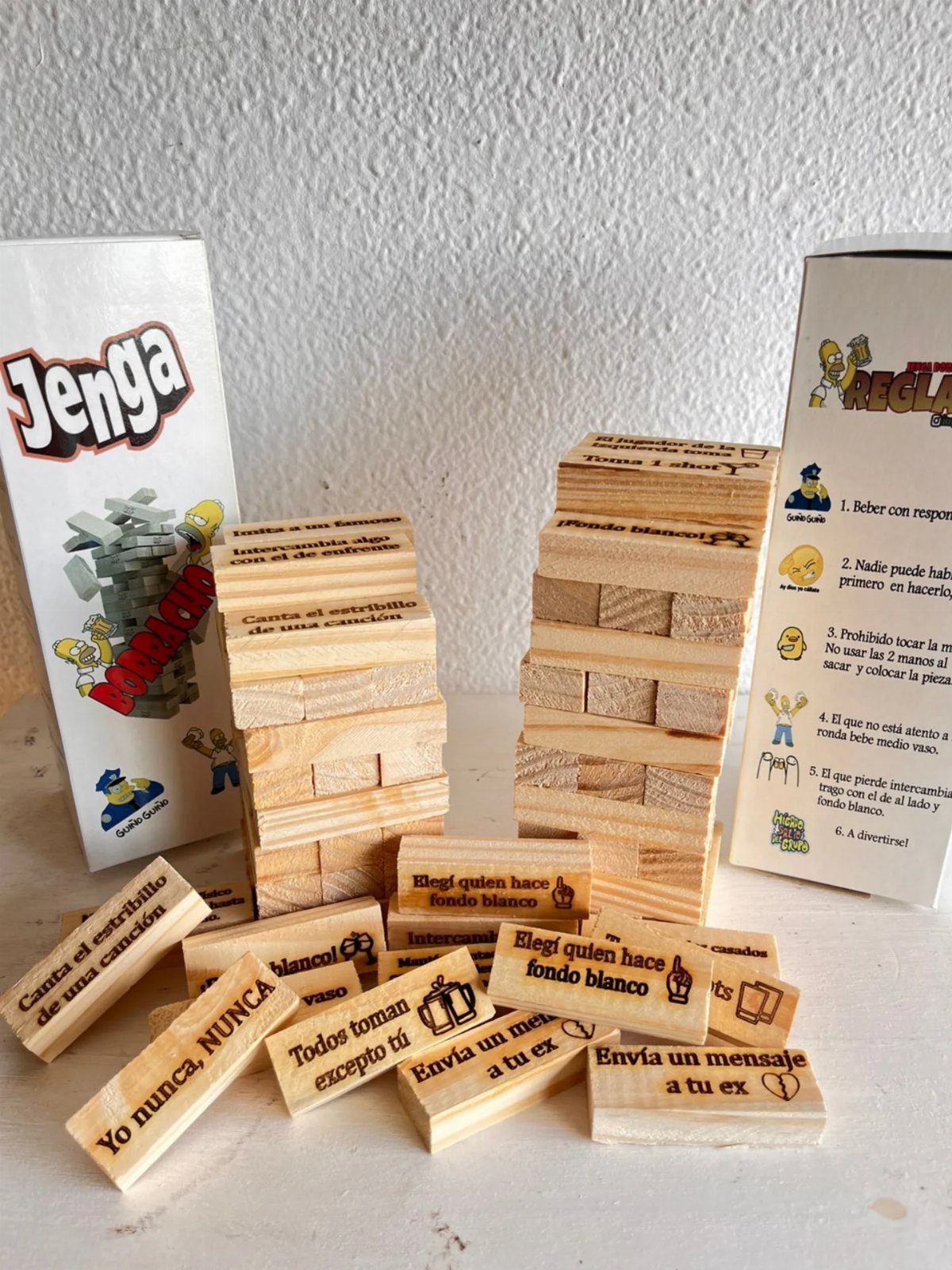 Wooden Jenga blocks with Spanish text scattered around two game boxes on a white surface.