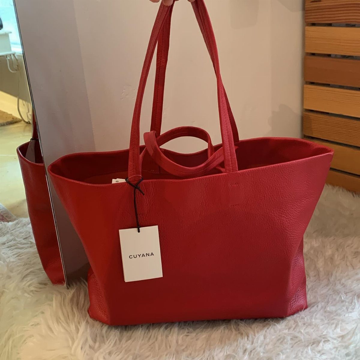 A bright red leather Cuyana tote bag sitting on a white faux fur rug.