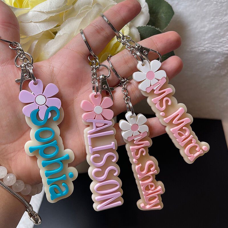A hand holding four colorful customized name keychains with flower decorations.