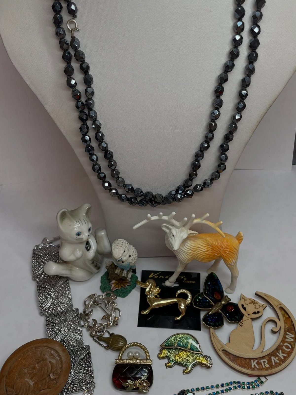 Assorted vintage jewelry and small figurines including a deer, a cat, and beaded necklaces on a white background.