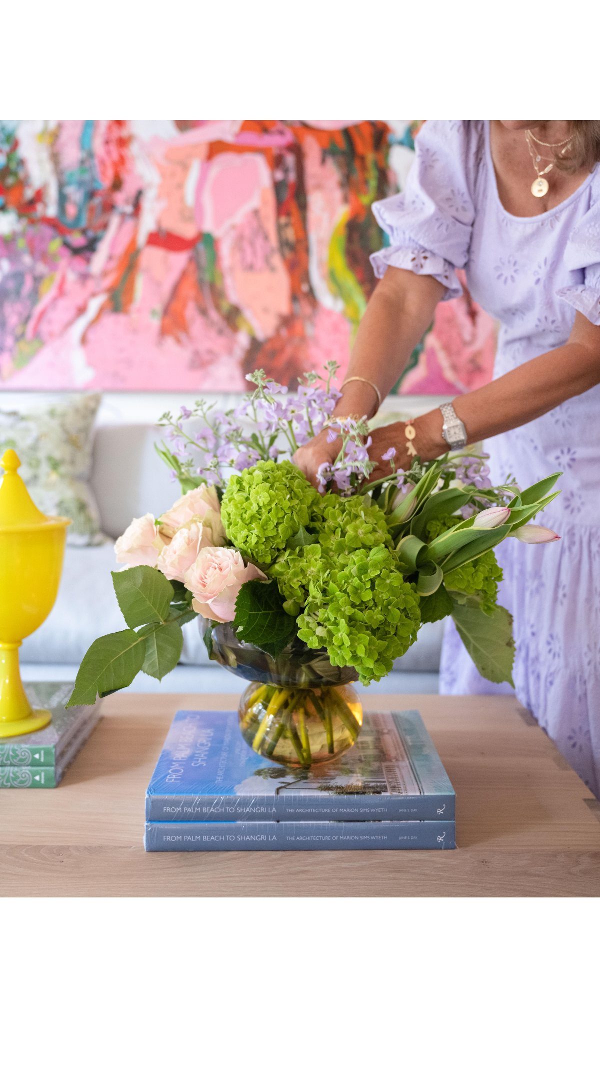 A person arranging a colorful floral bouquet in a decorative glass vase on a wooden table.