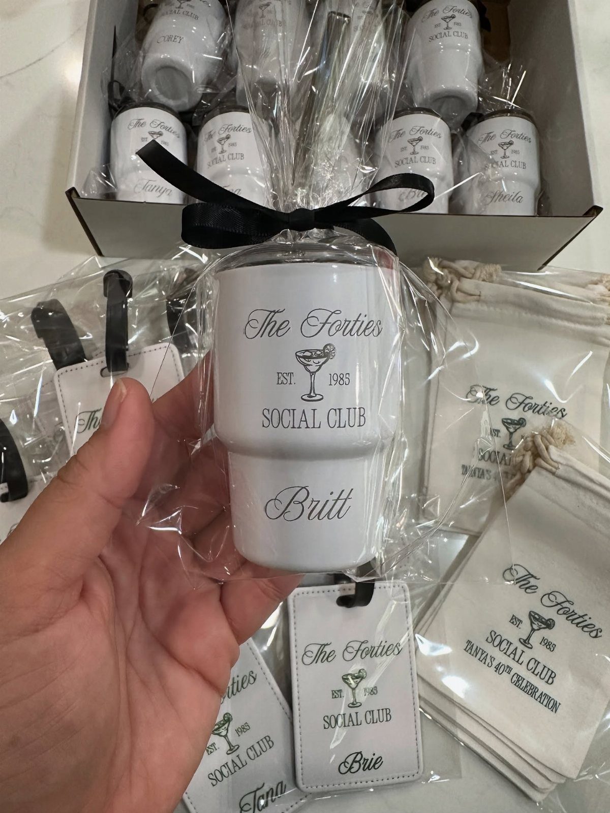 A hand holding a personalized white tumbler with black text and a black ribbon bow.