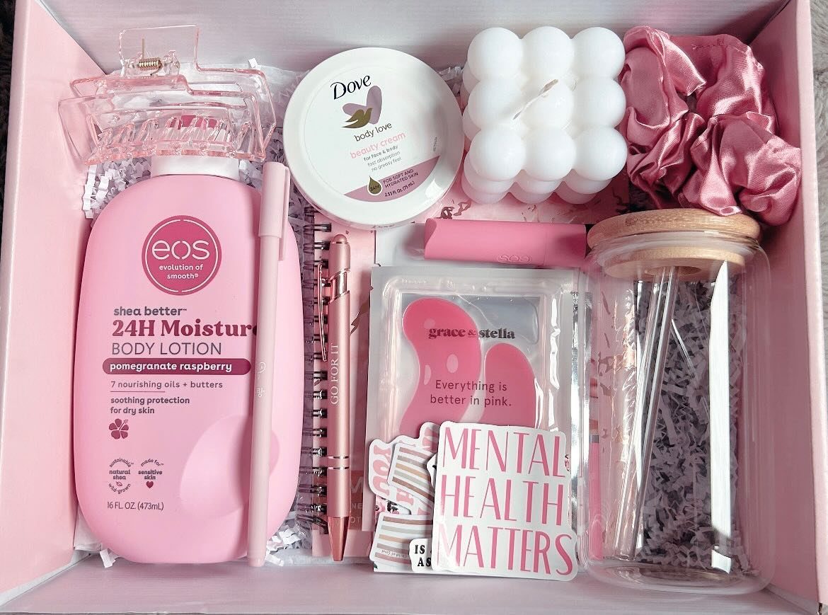A pink self-care gift basket containing body lotion, a bubble candle, a scrunchie, and skincare products.