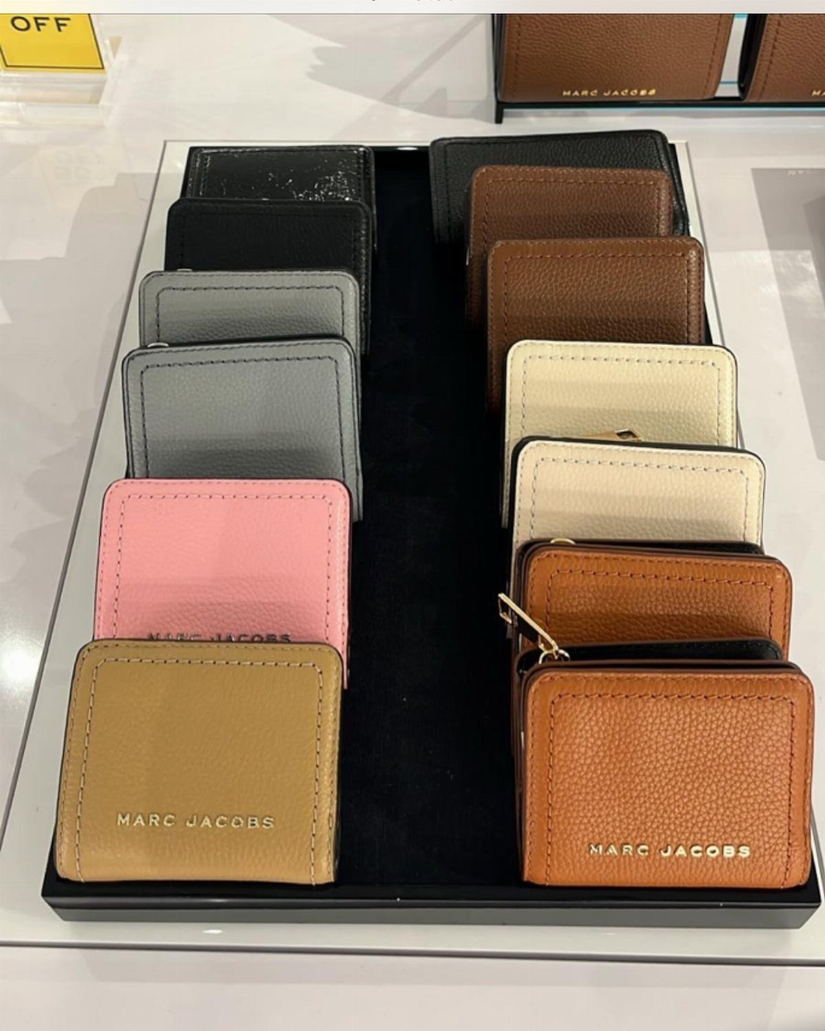 Multiple colorful Marc Jacobs leather wallets displayed in rows on a black tray.