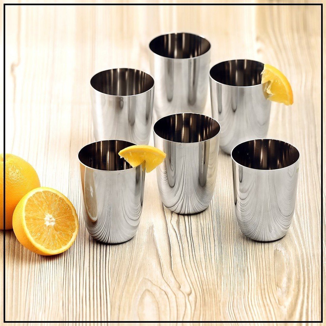 Six stainless steel shot glasses with orange slices on a light wooden table.