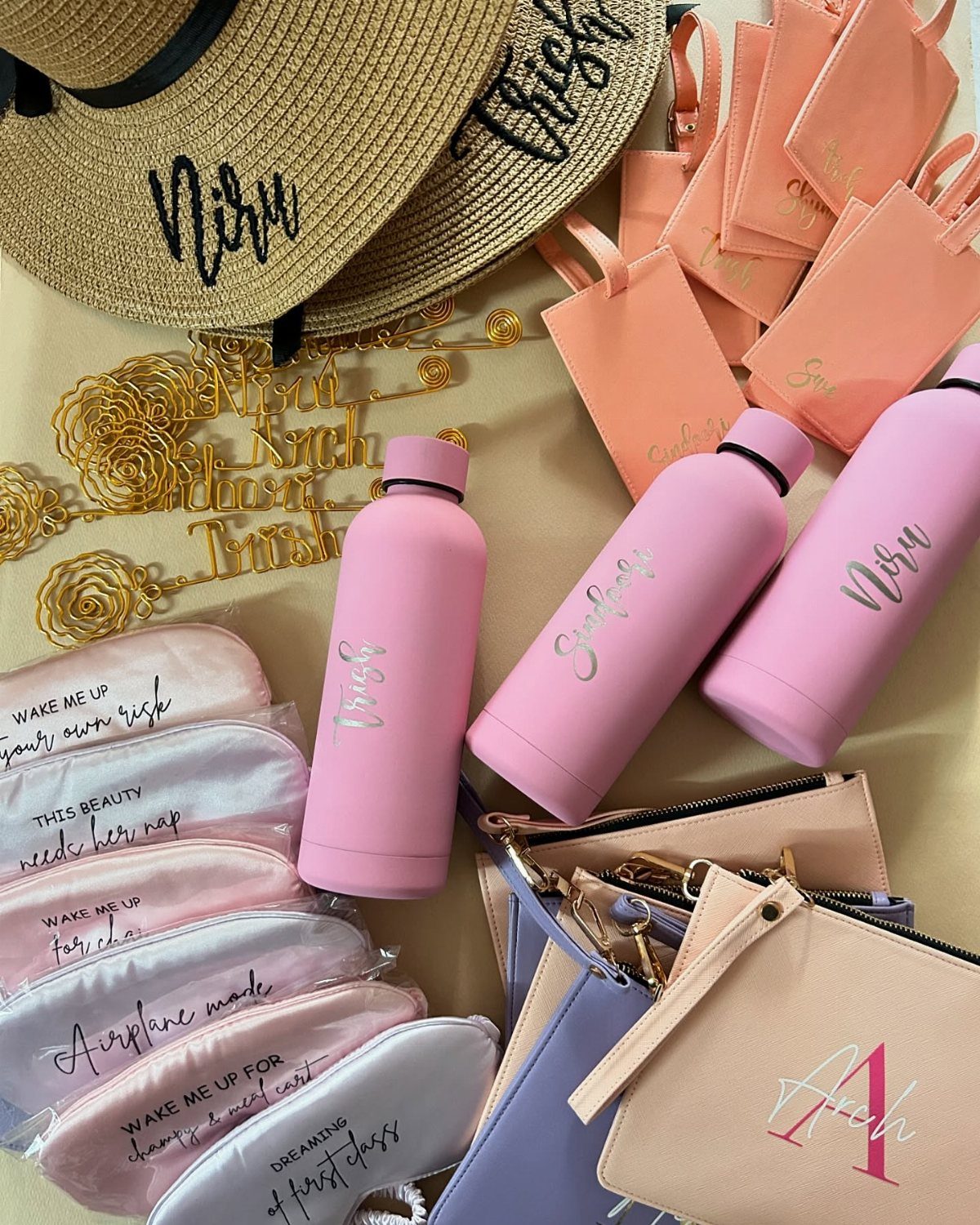 Pink water bottles, sleep masks, and a straw hat arranged as travel essentials.
