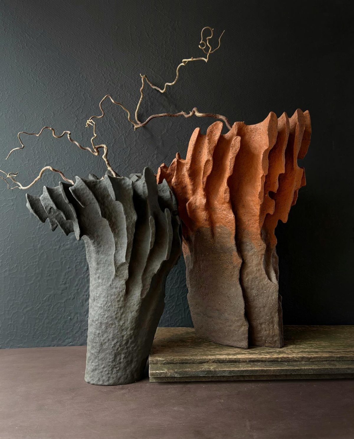 Two sculptural ceramic vases in grey and terracotta orange tones with a thin dry branch.
