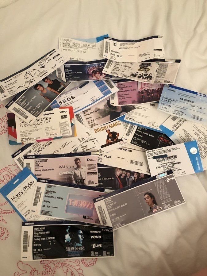 Numerous colorful concert tickets scattered across a white patterned bedsheet.