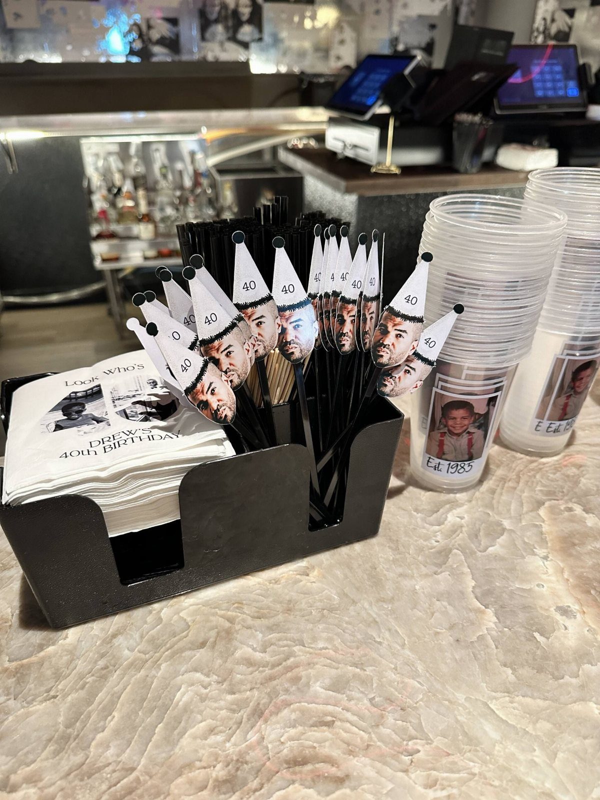 Party supplies including custom straws and cups with photos on a marble counter.
